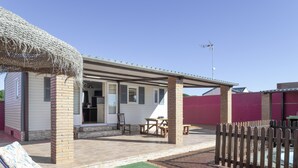 A covered patio area with a table and chairs, a lounge chair, and a brick pillar.