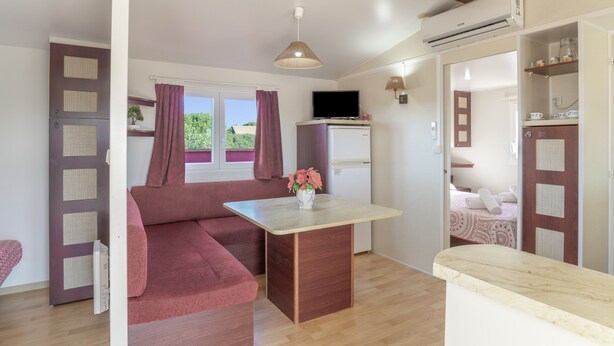 A room with a sofa, a small table, a TV, and an air conditioning unit.