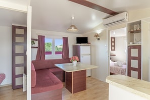 A room with a sofa, a small table, a TV, and an air conditioning unit.