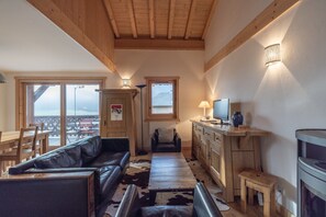 A cozy living area with a wooden ceiling, a leather sofa, a TV, and a dining table with chairs.