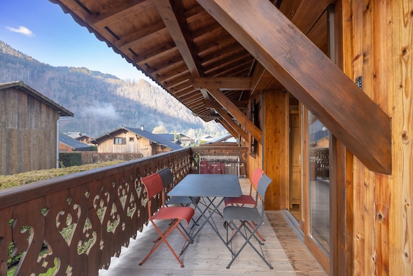 A wooden balcony with a table and chairs, overlooking a mountainous landscape.