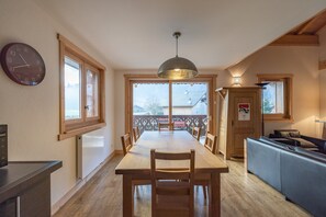 A dining area with a wooden table and chairs, a clock on the wall, and a view of the outside.