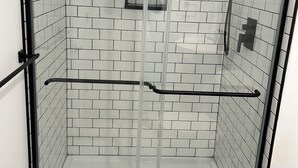 A glass-enclosed shower with white tiled walls and a black frame. - Cozy bed & breakfast in charming Ypsilanti with AC, WiFi (Ypsilanti)