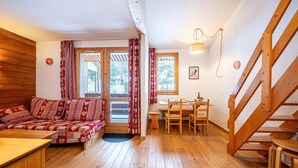 Una habitación acogedora con suelo de madera, un sofá con cojines estampados, una mesa de comedor con sillas y una escalera de madera.
