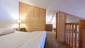 Un dormitorio con techo inclinado de madera, una cama, una mesita de noche, un aparador y una ventana.
