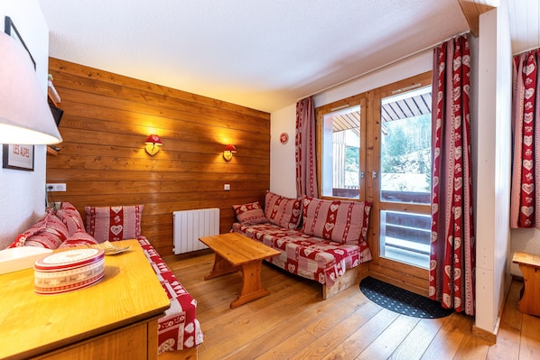 A cozy room with a wooden wall, a sofa, a table, and a window with curtains.
