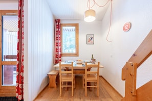 A wooden dining table with chairs, a bench, a window with curtains, a wall-mounted light, and a ski-themed picture.