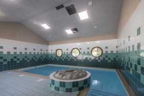 Piscina com hidromassagem circular no centro, rodeada por paredes revestidas e teto com iluminação embutida.