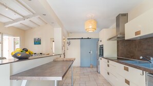 Une cuisine moderne avec un long plan de travail, un luminaire suspendu et une porte bleue en arrière-plan.