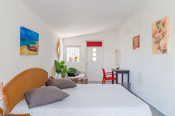 Une chambre à coucher avec un lit, un bureau, une chaise, une fenêtre et des œuvres d’art accrochées aux murs.