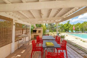 Une terrasse extérieure avec un barbecue, des chaises rouges et une piscine en arrière-plan.