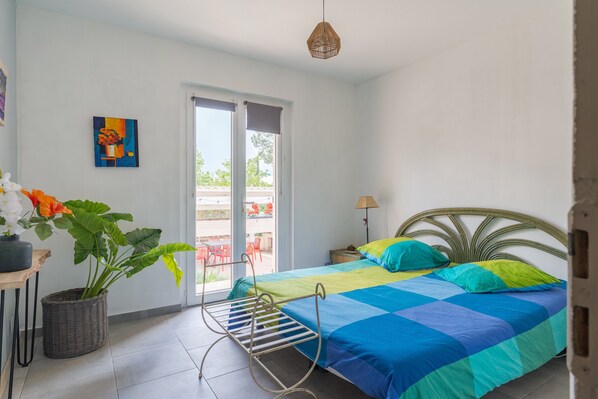 A bedroom with a bed, a potted plant, a metal drying rack, a painting, and a view through a door. - Traditional House 'Coeur De Lavande' with Private Pool, Enclosed Garden, and Wi-Fi (Vinon-sur-Verdon)