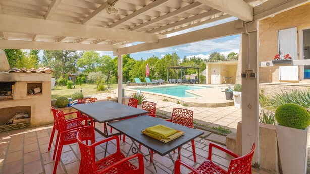 Une terrasse extérieure avec une piscine, des chaises rouges et une table.