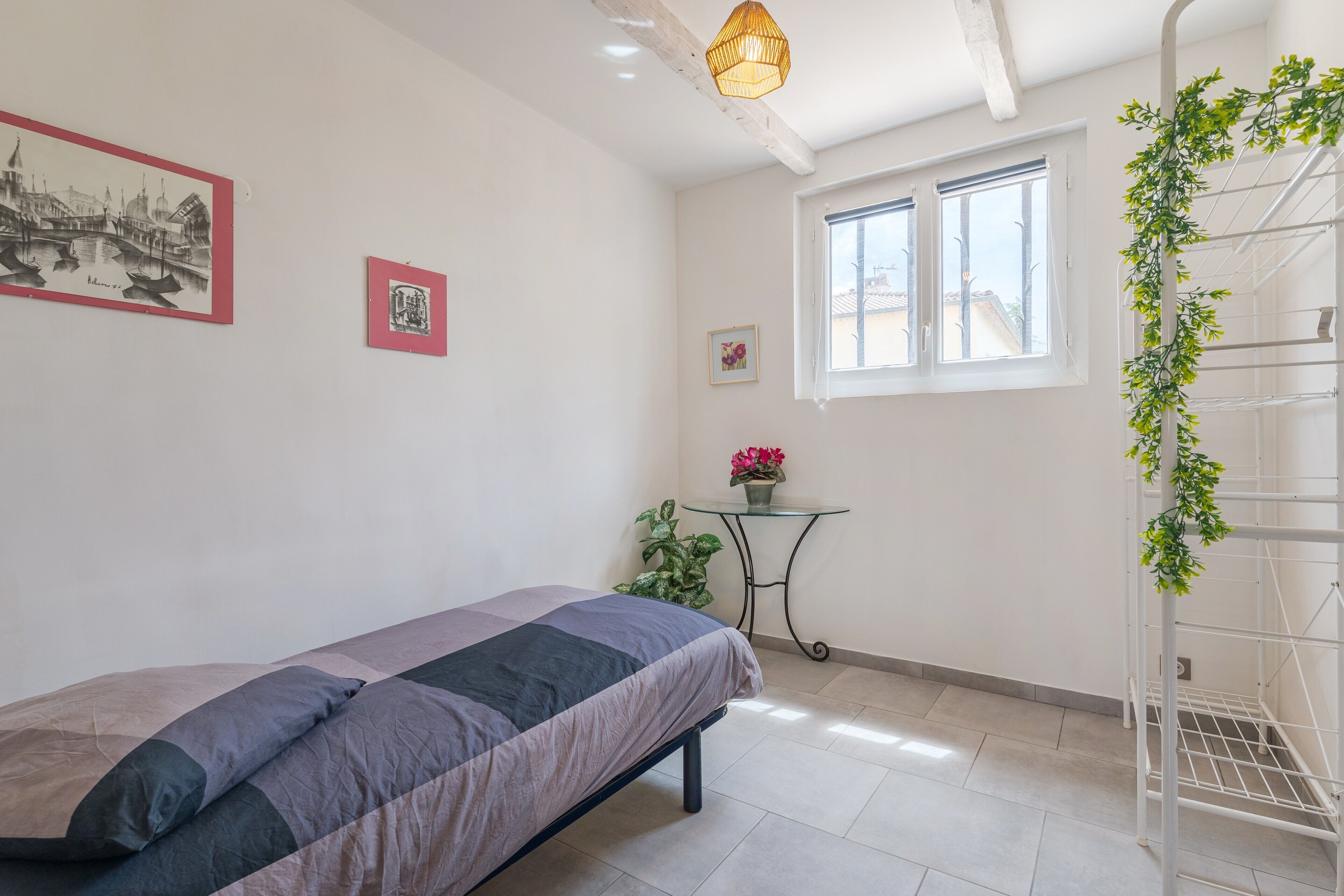 Ein Schlafzimmer mit Bett, Fenster, Pflanze und Wandregal.