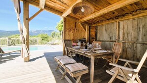 Une terrasse en bois avec une piscine, une table dressée pour le repas et une vue sur les montagnes.