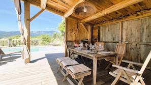 Un terrazza in legno con piscina, un tavolo apparecchiato per mangiare e vista sulle montagne.