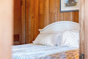 Ein Bett mit weißer Bettwäsche in einem Zimmer mit Holzwandverkleidung.