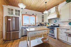 A kitchen with wooden cabinets, stainless steel appliances, a central island, and pendant lighting. - Resting Beach Face: Semi-Oceanfront, Classic Nags Head Flat Top Home, Private Pool, Hot Tub (Nags Head)