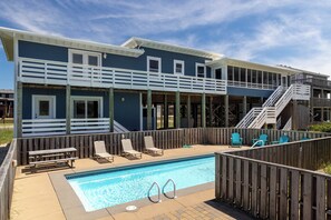A pool area with a wooden deck, lounge chairs, and a staircase leading to an upper level. - Resting Beach Face: Semi-Oceanfront, Classic Nags Head Flat Top Home, Private Pool, Hot Tub (Nags Head)