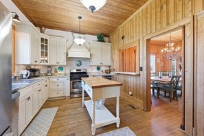 Una cocina con armarios blancos, techo de madera y un comedor con candelabro.