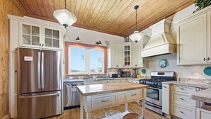 Une cuisine dotée de meubles en bois, d’appareils électroménagers en acier inoxydable, d’un îlot central et de luminaires suspendus.