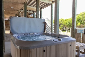 Un bain à remous situé sous une structure en bois, avec un panneau indiquant qu’il faut prendre une douche avant d’entrer dans la piscine.