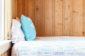 Una pared de madera, una cama con un edredón estampado y dos almohadas.
