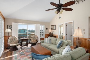 A spacious living room with a ceiling fan, a large window with shutters, a sofa set, and a patterned rug.