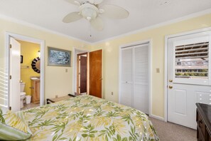 A bedroom with a bed, a ceiling fan, a door with blinds, and a window with a view of buildings.