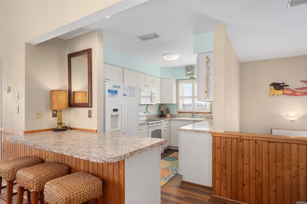 A kitchen with white cabinets, a granite countertop, and a wooden island with bar stools. - Hawk's Nest: Semi-Oceanfront, Hot Tub, Close to Beach Access (Nags Head)