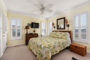 A bedroom with a bed, a ceiling fan, a television, a dresser, and a window with shutters. - Hawk's Nest: Semi-Oceanfront, Hot Tub, Close to Beach Access (Nags Head)
