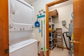 A laundry area with a washer and dryer, a broom, and a ladder. - Hawk's Nest: Semi-Oceanfront, Hot Tub, Close to Beach Access (Nags Head)