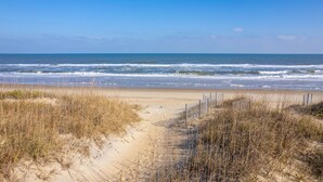 Un sentier qui longe la plage et mène à l’océan, avec des dunes et une clôture en bois.