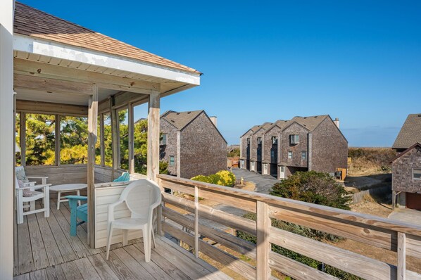 A wooden deck with outdoor furniture, a covered area, and a view of multiple houses with similar architecture. - Hawk's Nest: Semi-Oceanfront, Hot Tub, Close to Beach Access (Nags Head)