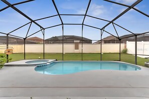 Ein Schwimmbad mit Glasveranda, umgeben von einer Rasenfläche und einem weißen Zaun.
