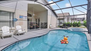 En swimmingpool med solstolar och ett bubbelbad, omgivet av en täckt uteplats.