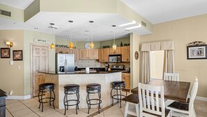 A kitchen with a central island, bar stools, a dining table with chairs, and various kitchen appliances.