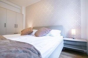 Un dormitorio con cama, almohadas, una mesita de noche con lámpara y un armario.