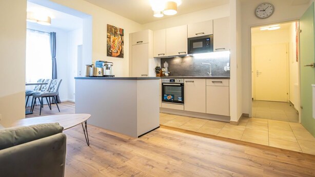 Una cocina compacta con microondas, horno y una pequeña isla. Hay un comedor con sillas y una mesa.