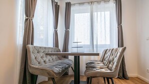 Un comedor con una mesa y dos sillas tapizadas, una ventana con cortinas y suelo de madera.