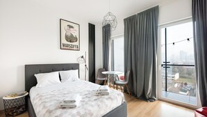 A modern hotel room with a large bed, a small round table, and a city view.