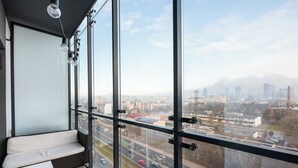 A modern room with a large window, a white bench, and a view of a cityscape.
