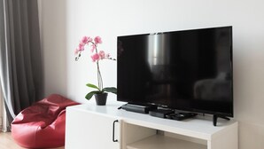 A modern living room with a flat-screen TV on a white cabinet, a red bean bag chair, and a potted orchid plant.