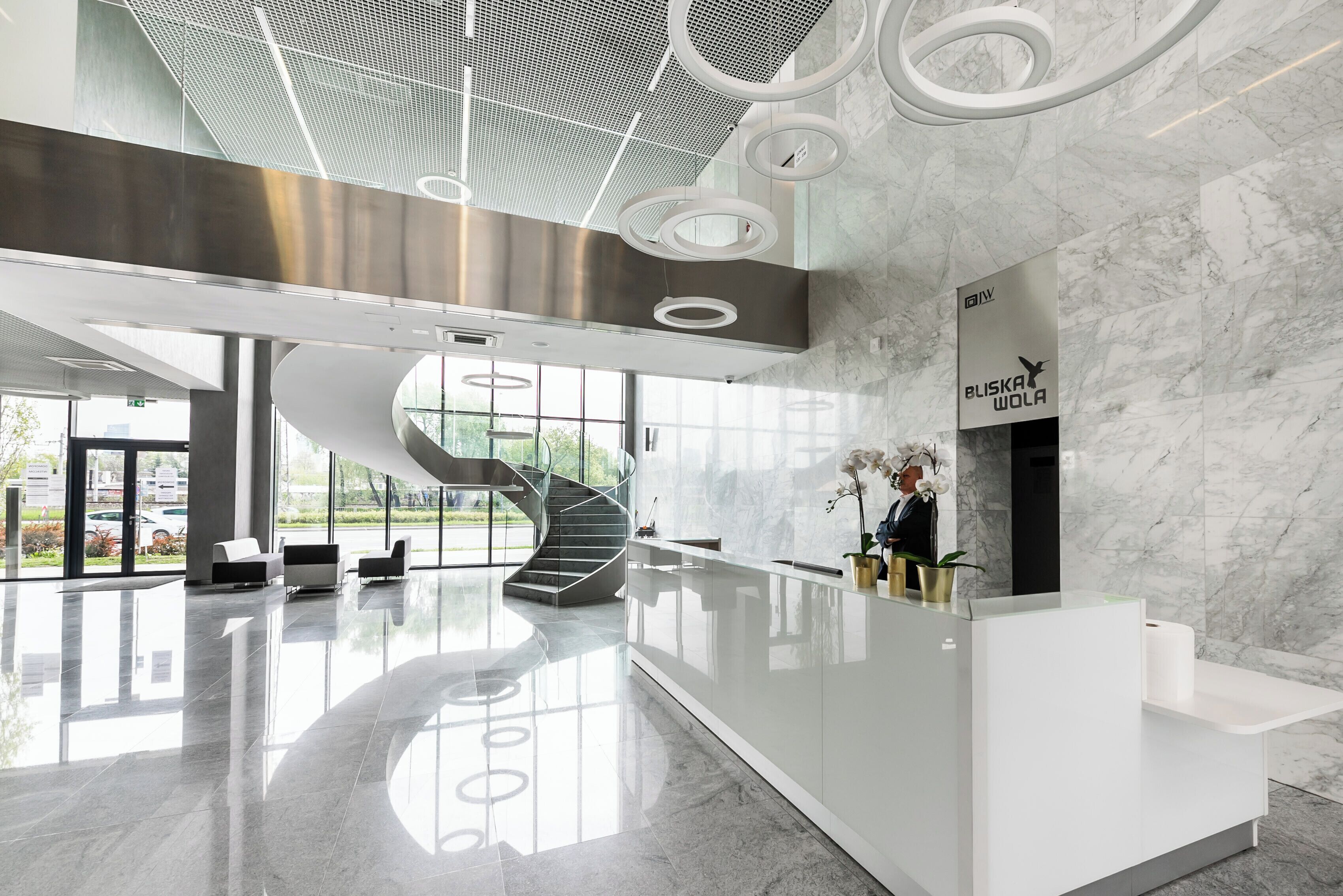 Un moderno vestíbulo de hotel con una escalera espiral central, una recepción y un amplio ventanal con vistas al exterior.