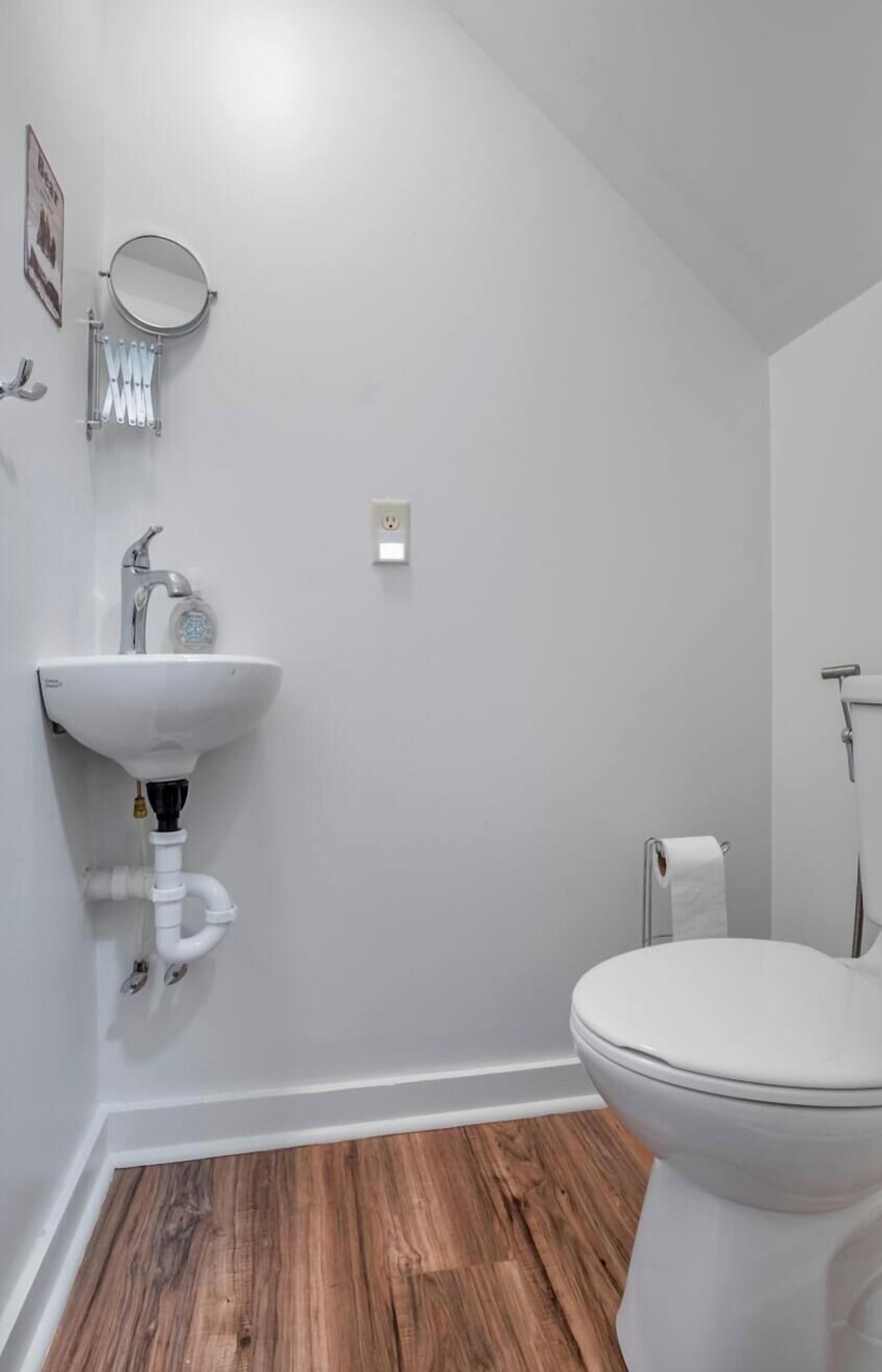 Een badkamer met een witte wastafel, toilet en houten vloer.