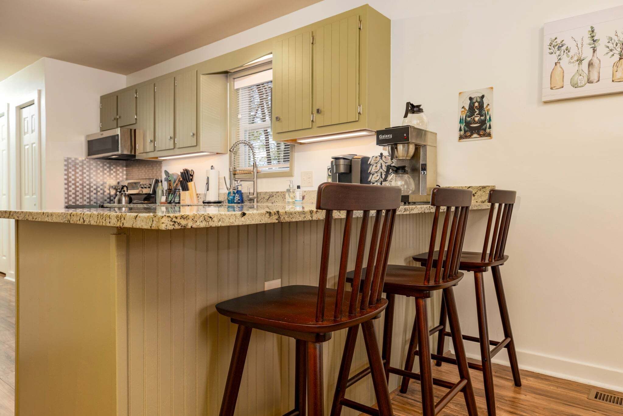 A kitchen with wooden cabinets, a bar area with stools, a coffee machine, and a microwave.