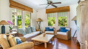 Una habitación luminosa con muebles de mimbre, ventanas amplias y ventilador de techo.