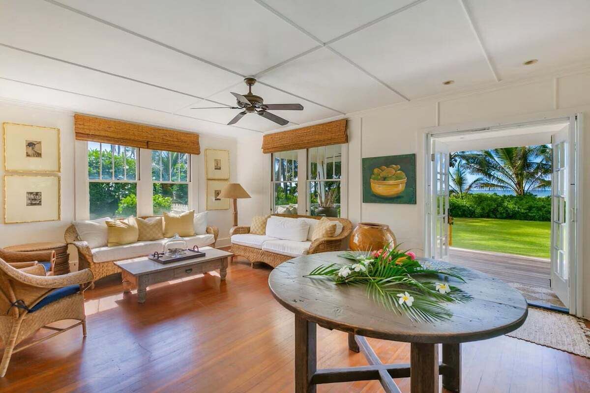 A spacious living room with a large window, a ceiling fan, and a view of a lush garden.