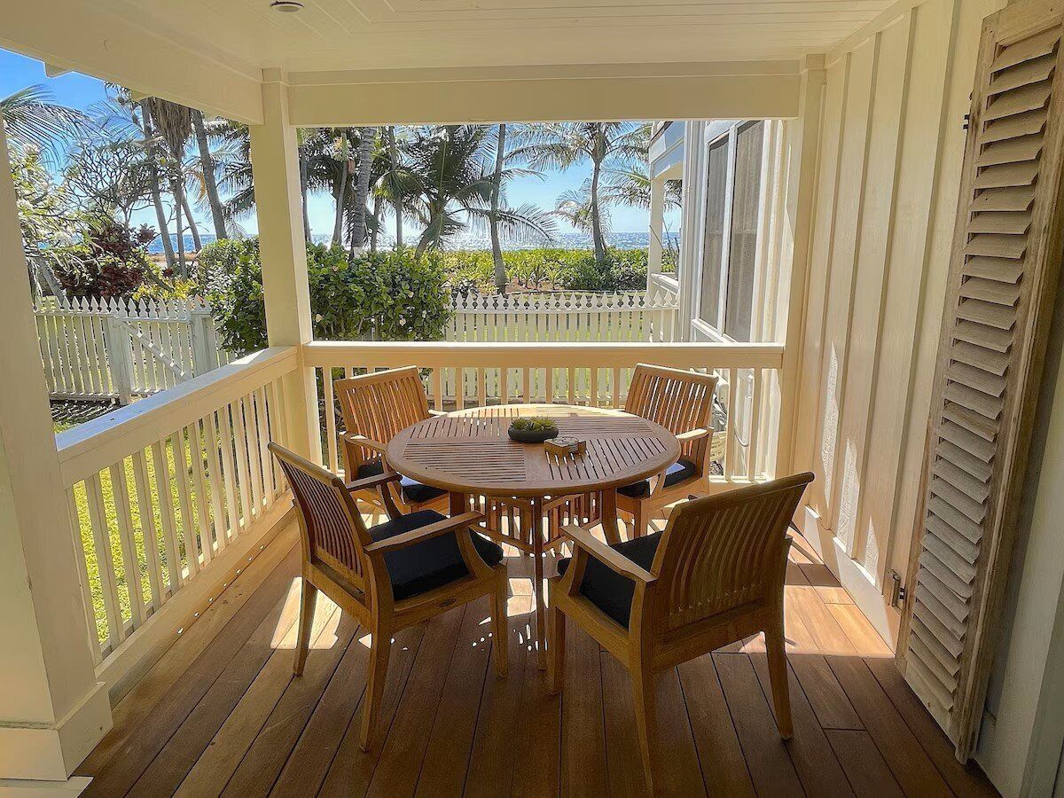 A covered outdoor patio with a round wooden table and six chairs, surrounded by a white picket fence.