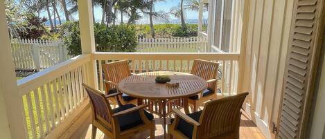 A covered outdoor patio with a round wooden table and six chairs, surrounded by a white picket fence.